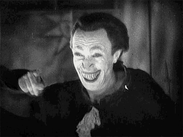 a black and white photo of a man wearing a clown costume and smiling .