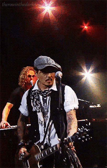 a man playing a guitar and singing into a microphone with the words " theroseinthedark " on the bottom right