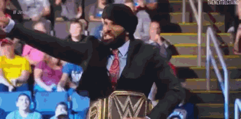 a man in a suit and tie is holding a wrestling championship belt in a stadium .