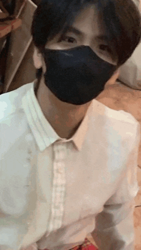a man wearing a white shirt and a black mask is sitting on the floor .