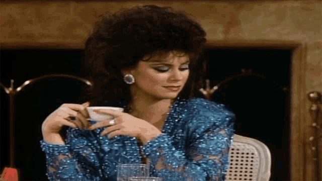 a woman in a blue dress is holding a cup and a cigar