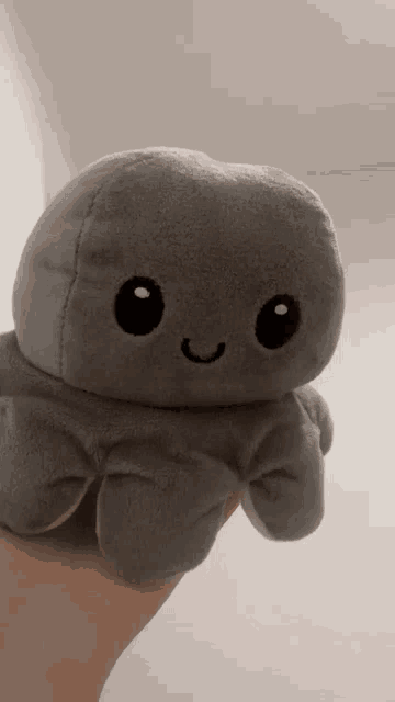 a person is holding a gray octopus stuffed animal with a smiling face .