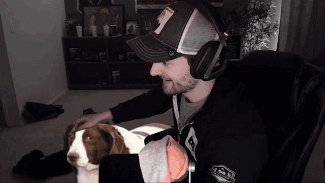 a man wearing headphones and a hat that says ' goat ' on it is petting a brown and white dog