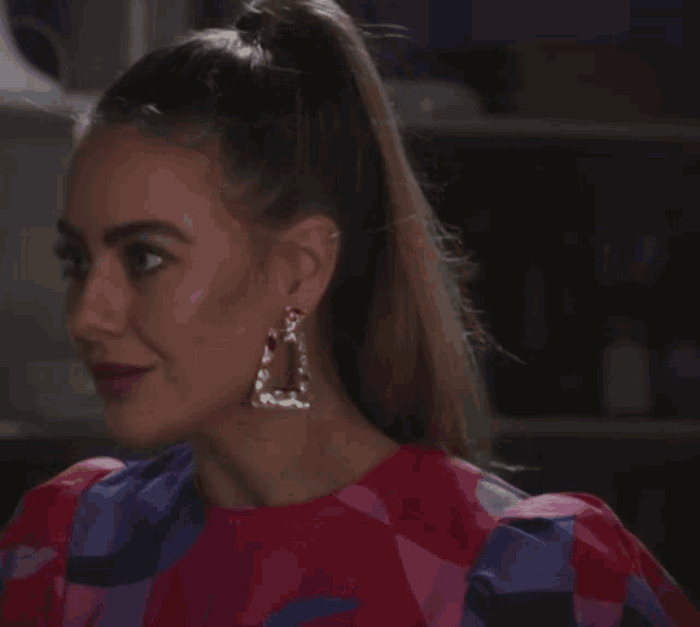 a woman wearing a ponytail and earrings looks to the left