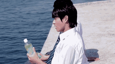 a young man in a tie is sitting on a dock holding a bottle of water .