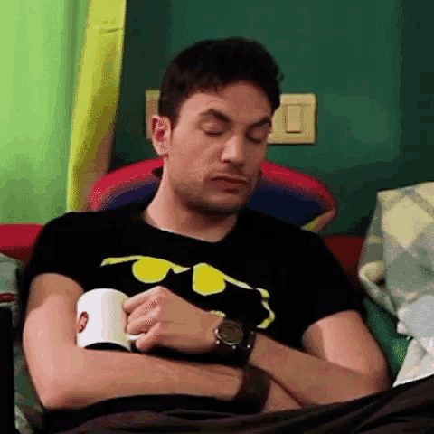 a man wearing a batman shirt is sleeping on a couch with his eyes closed