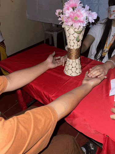 a vase of pink flowers sits on a table with two people holding hands
