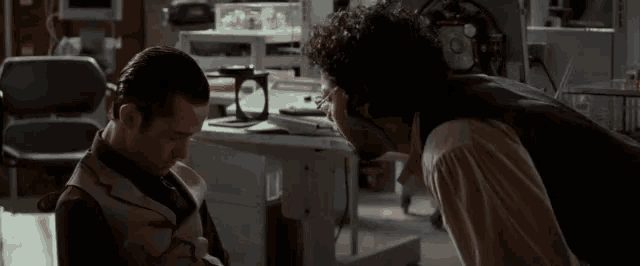two men are standing next to each other in a room talking to each other .