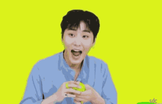a young man in a blue shirt is holding a yellow object in his hands against a yellow background .