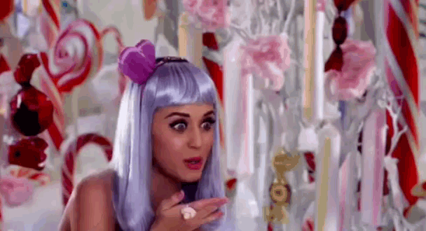 a woman in a purple wig is blowing a kiss in front of a candy cane display .