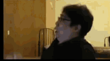 a woman wearing glasses is standing in a room with a bed in the background .
