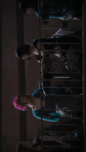 a man and a woman are looking at each other in a dark room with a red exit sign in the background