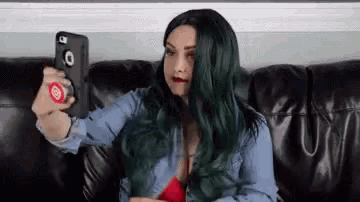 a woman with green hair is taking a selfie with her cell phone .