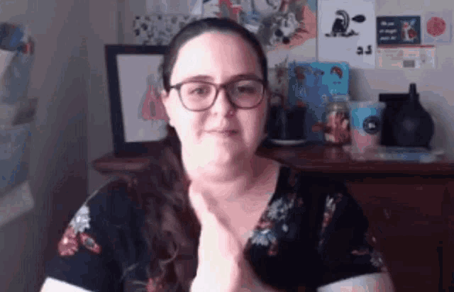 a woman wearing glasses and a floral shirt is giving a thumbs up sign .