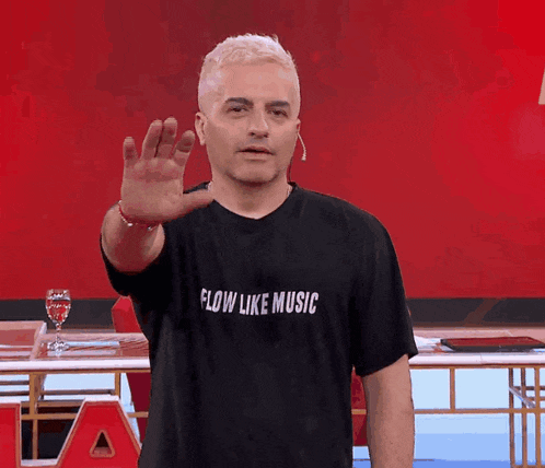 a man wearing a flow like music t-shirt waves his hand