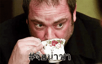 a man is drinking a cup of tea with a foreign language written on it .