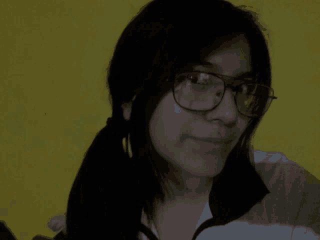 a woman wearing glasses and pigtails looks at the camera with a yellow background
