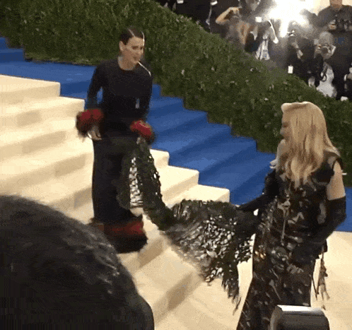 a woman in a black dress is walking down stairs next to another woman