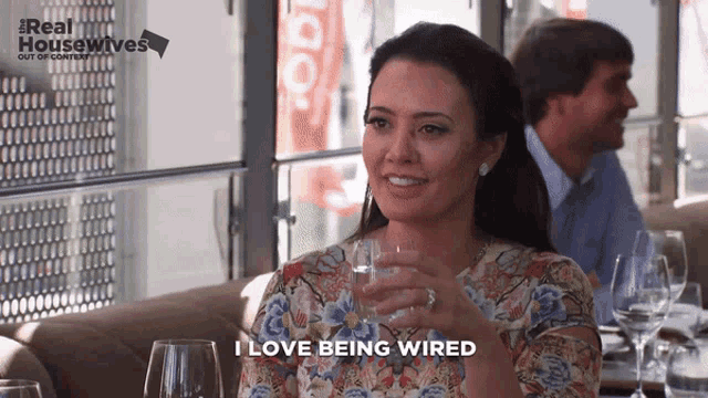 a woman sitting at a table with a glass of water and the words " i love being wired " next to her