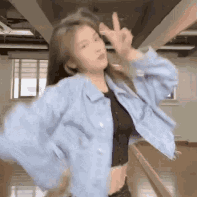 a woman wearing a blue jacket and a black crop top is making a peace sign .
