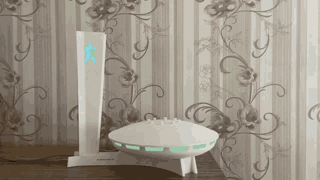 a white device with a green star on top of it sits on a table in front of a floral wallpaper