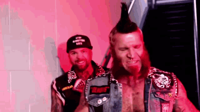 a man with a mohawk and a beard is standing next to another man with a beard .