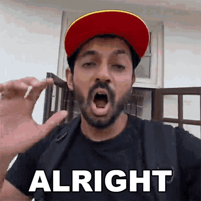 a man with a beard wearing a red and yellow hat says " alright "
