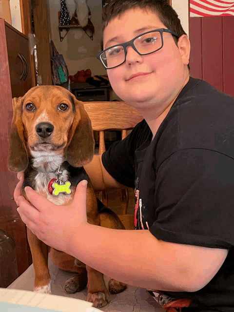 a boy wearing glasses is holding a dog with a tag that says ' snoopy ' on it