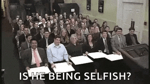 a large group of people are sitting in a room holding papers with the words `` is he being selfish '' written above them .