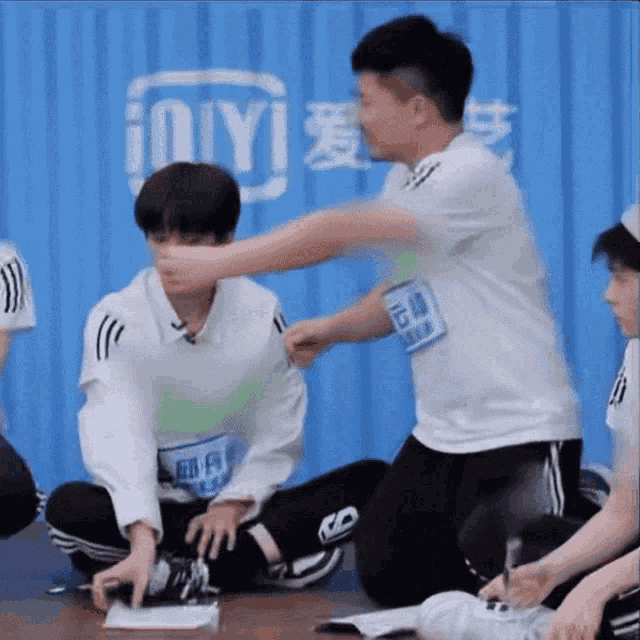 a group of young men are sitting on the floor and one of them has an ioiyi tag on his shirt