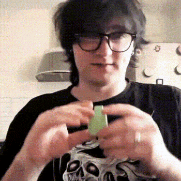 a man wearing glasses and a black shirt with a skull on it is holding something in his hands .