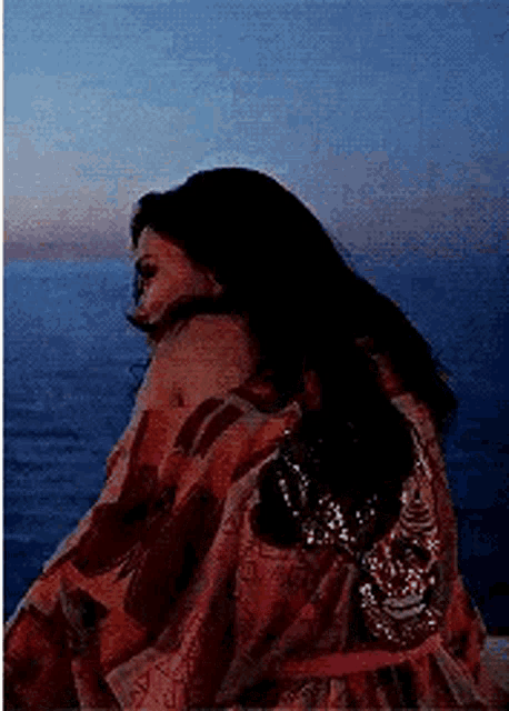 a woman in a red dress is sitting on a beach looking at the ocean .