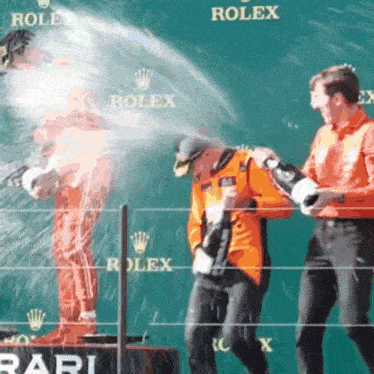 a man is spraying champagne on another man in front of a rolex sign