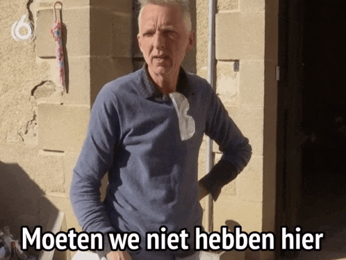 a man in a blue shirt is standing in front of a brick wall with the words moeten we niet hebben hier written below him