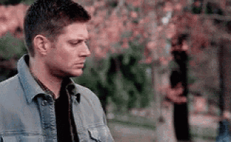 a man wearing a denim jacket is standing in a park .