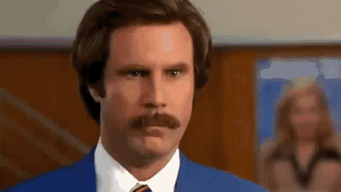 a man with a mustache is wearing a blue suit and tie and looking at the camera .