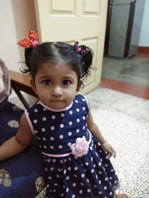 a little girl wearing a blue polka dot dress with a pink flower on the waist