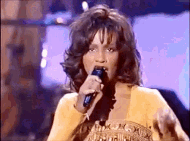 a woman is singing into a microphone while wearing a yellow dress .