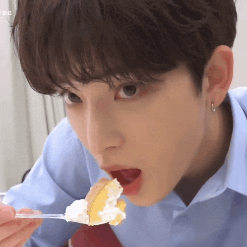 a young man in a blue shirt is eating a piece of cake