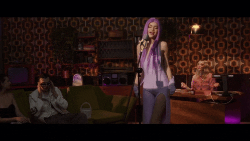 a woman with purple hair singing into a microphone in a room