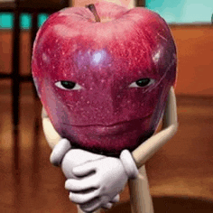 a red apple with a face on it is being held by a person with gloves .