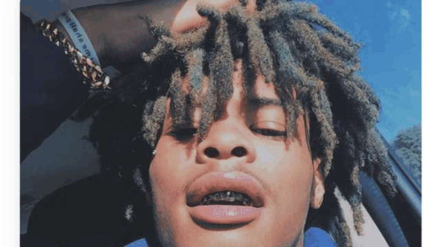 a man with dreadlocks has a bracelet on his wrist that says " brilliant a genius "