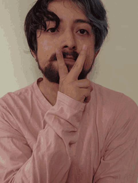 a man with a beard and blue hair is wearing a pink shirt and covering his mouth with his hand