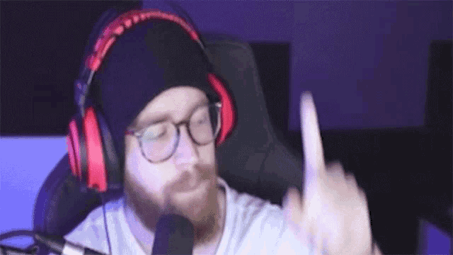 a man with a beard wearing headphones and glasses is sitting in front of a microphone .