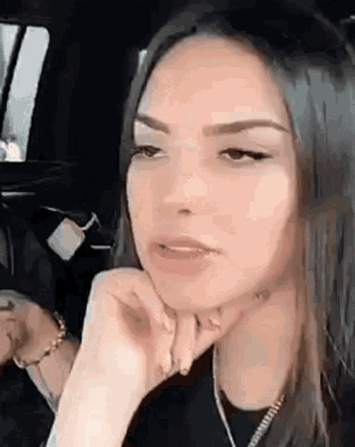 a woman is sitting in a car with her hand on her chin and looking at the camera .