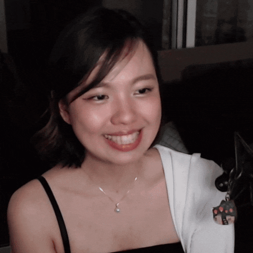 a woman wearing a black tank top and a necklace smiles