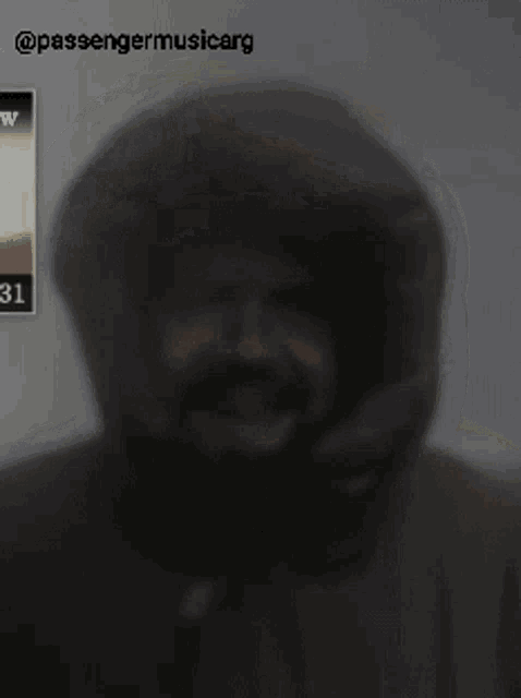 a man wearing a hooded jacket is smiling in front of passengermusicarg