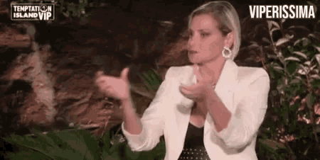 a woman in a white jacket is clapping her hands while standing in front of a waterfall .