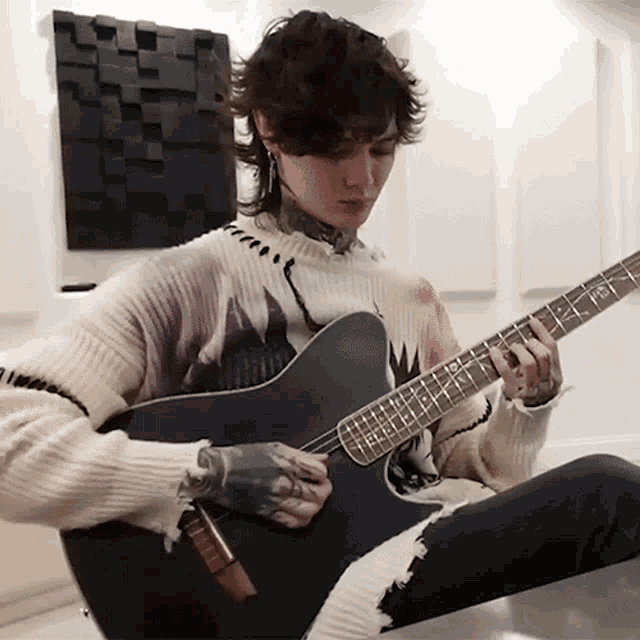 a man in a sweater is playing a guitar with the letter g on the neck