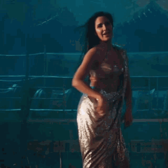 a woman in a silver saree is dancing in a room with lights .
